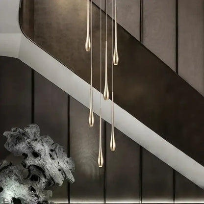 Five slender teardrop pendant lights with brushed gold finish hang vertically in decorbites gold-plated modern chandeliers