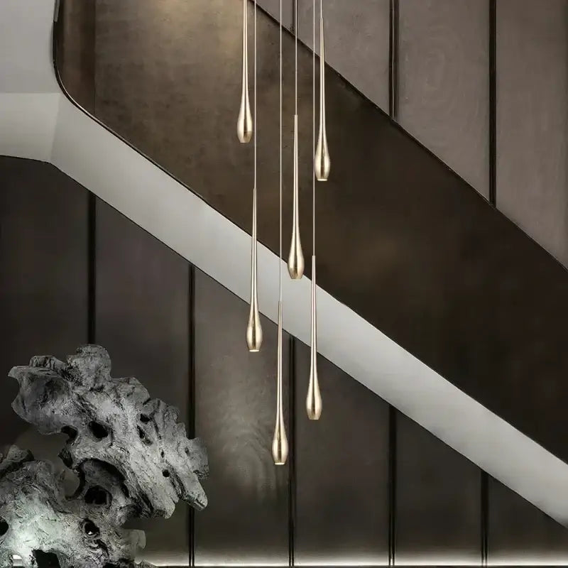 Five slender teardrop pendant lights with brushed gold finish hang vertically in decorbites gold-plated modern chandeliers