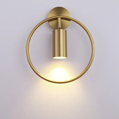 Gold-toned modern wall sconce light with a sleek cylindrical LED fixture and polished metal ring for bedroom use