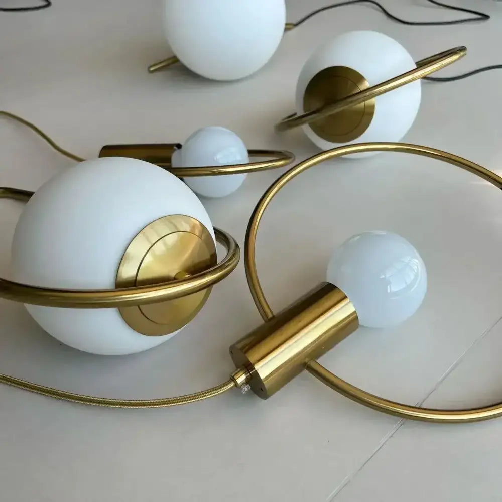 Modern gold ring pendant light featuring white frosted glass globes with gold-toned rings and cylindrical bases