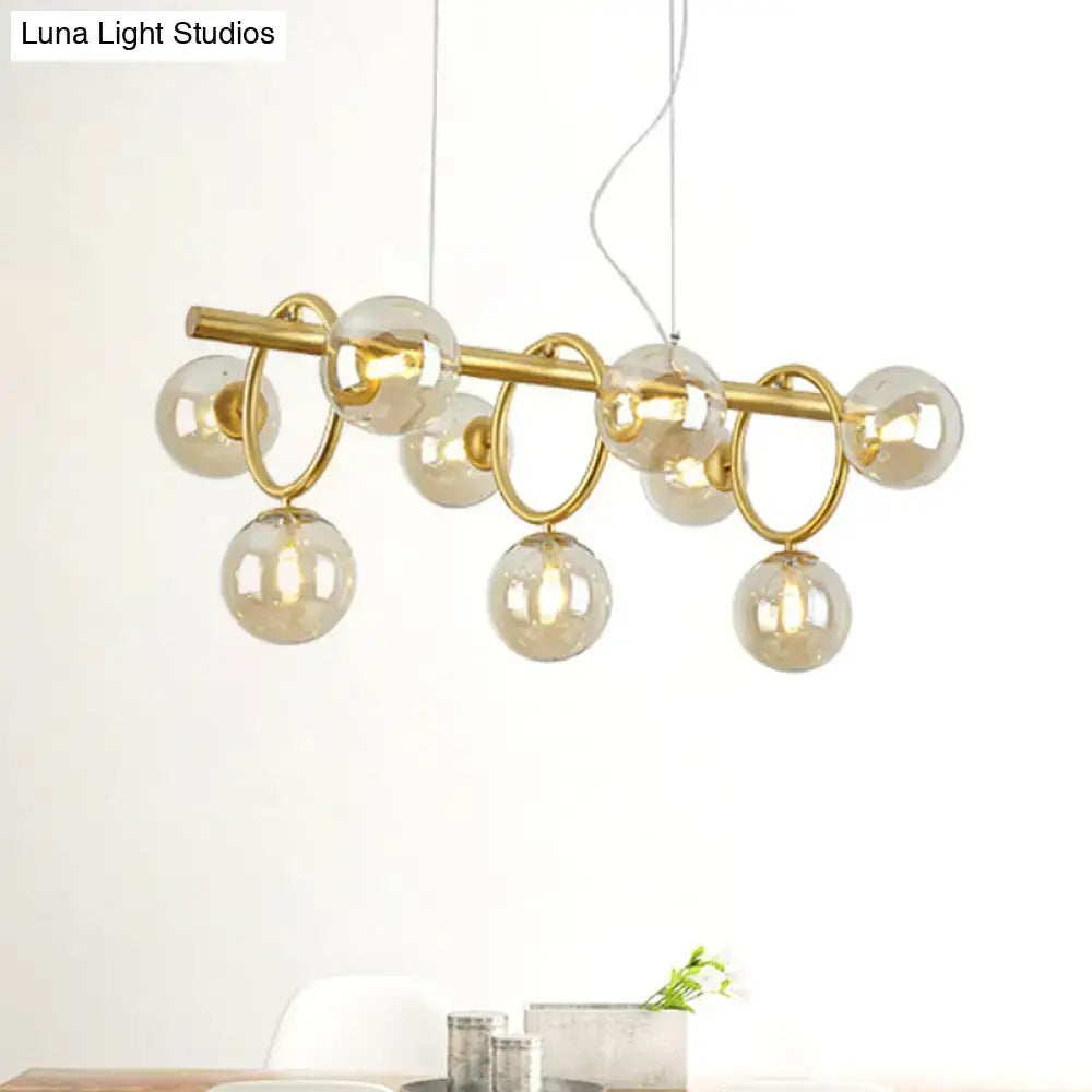 Modern gold round pendant chandelier with cognac glass spheres and linear design in a dining room setting