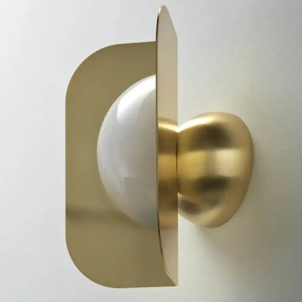 Modern gold sconce light with curved metal shade and frosted glass globe designed as a bedroom lamp wall fixture