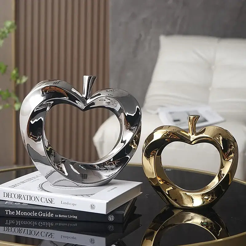 Two glossy ceramic apple sculptures in polished gold and reflective silver rest elegantly on a glass table for decor