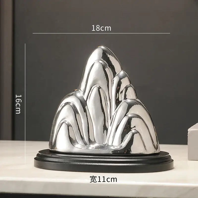 Shiny silver metallic ceramic mountain sculpture with smooth flowing contours on black base decorbites ceramic mountain decor