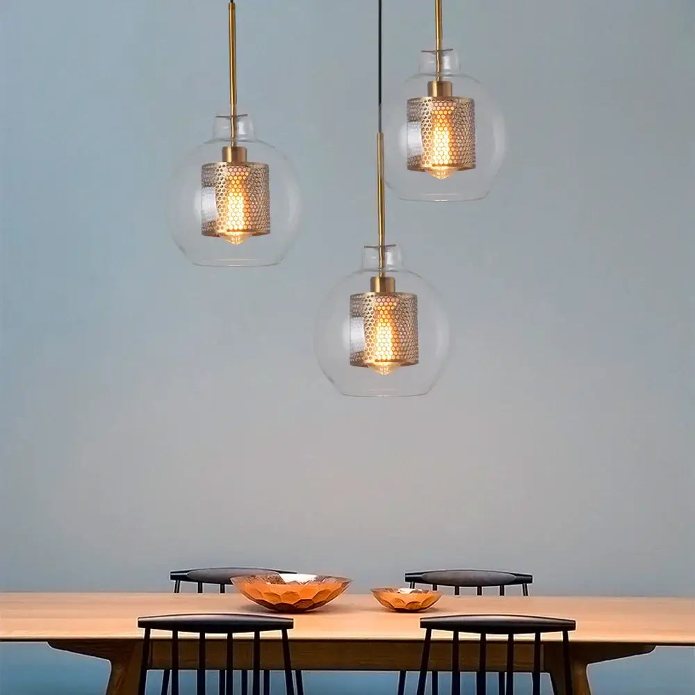 Three modern gold and silver honeycomb mesh glass pendant lights with clear ball glass pendants above dining table