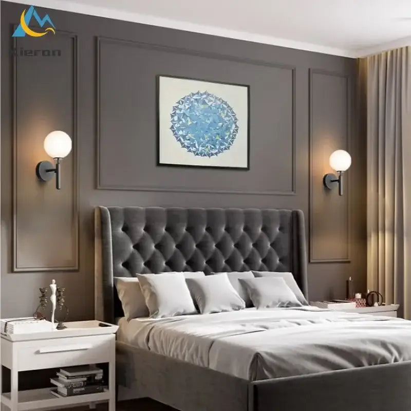Modern gold spherical frosted glass led wall lamps installed above a gray tufted velvet bed with matching bedding and white pillows