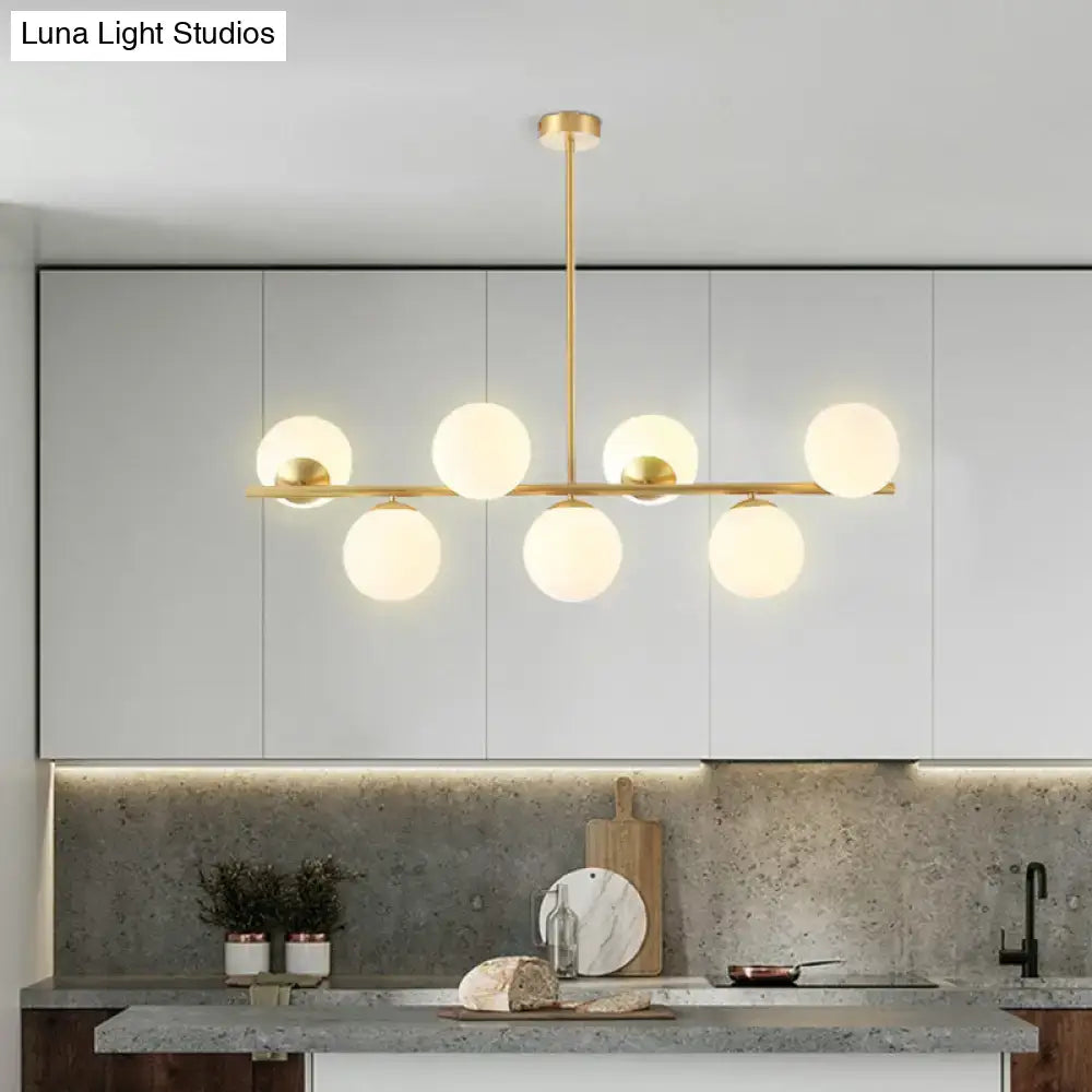 Modern gold-toned island ceiling light with six frosted glass globes in a linear pendant lighting design