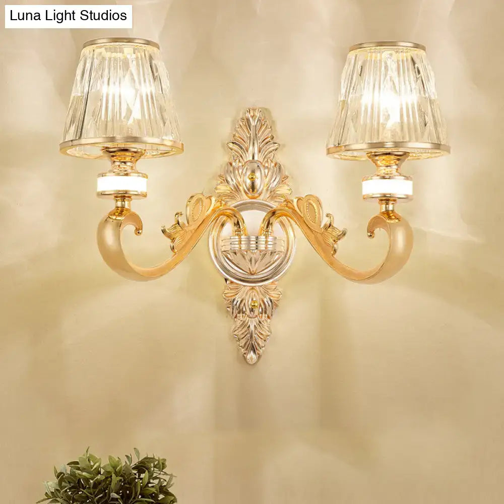 Modern gold wall lamp fixture with two crystal cone shades and intricate leafy gold wall detailing for bedroom sconce