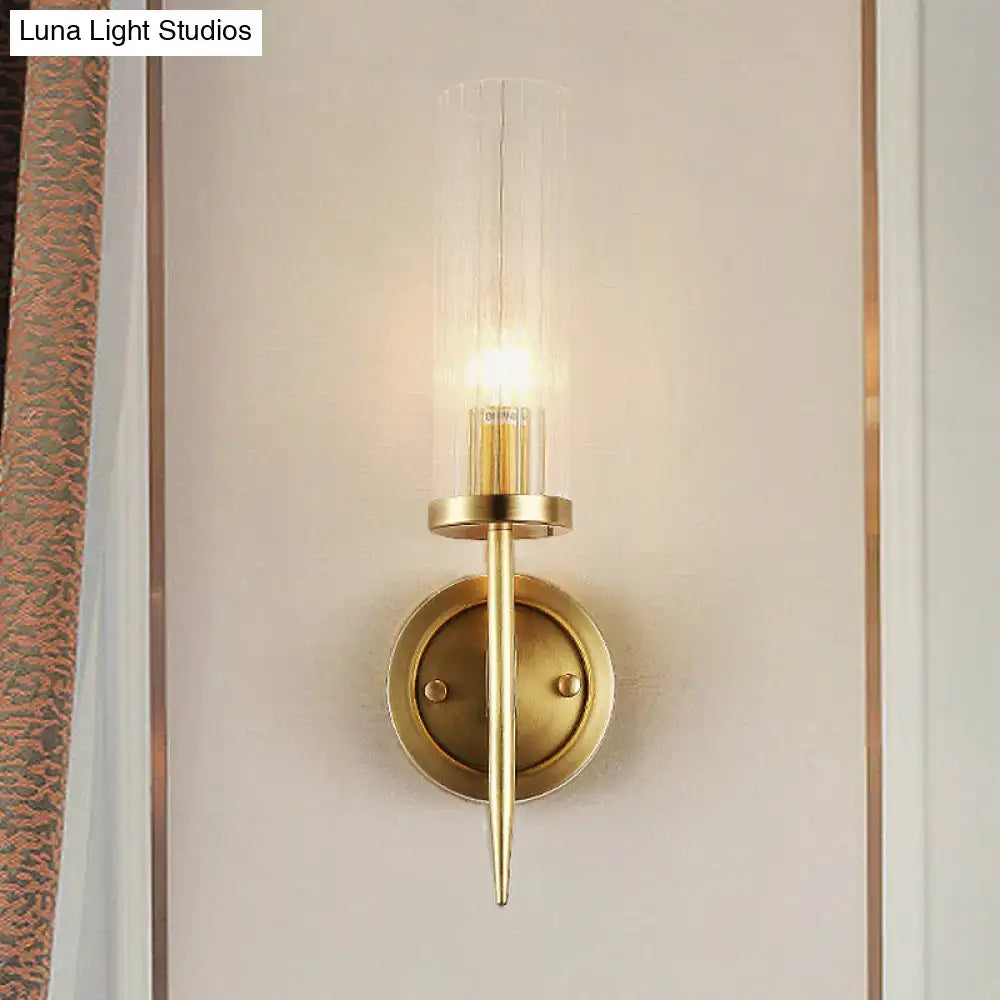 Modern gold wall sconce with clear ribbed glass cylinder housing an illuminated led bulb for 110v-120v use