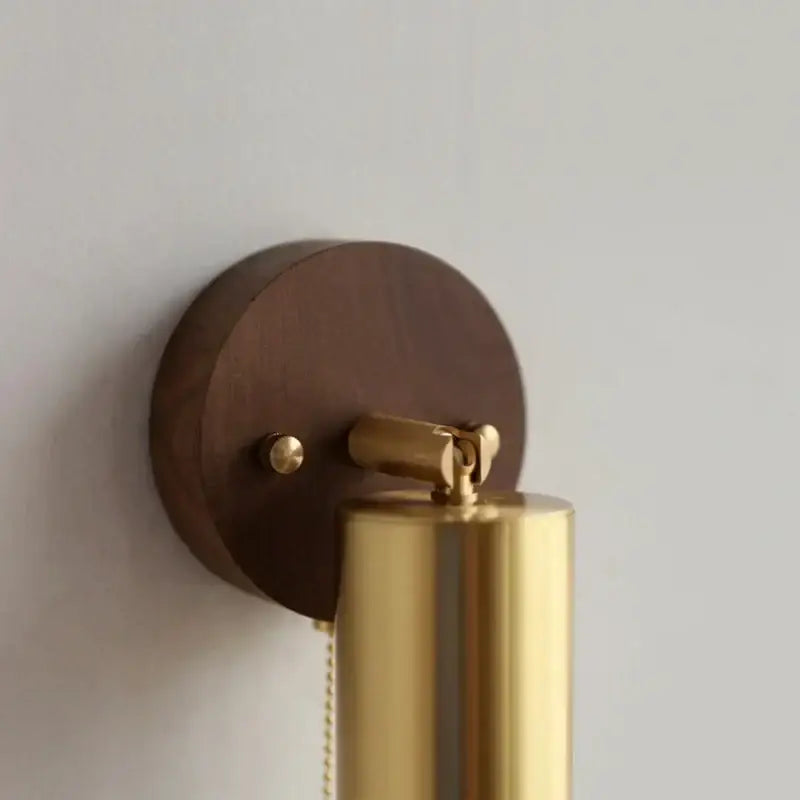 Modern gold walnut wall sconce with pull chain switch featuring a sleek brass design and dark wood circular base