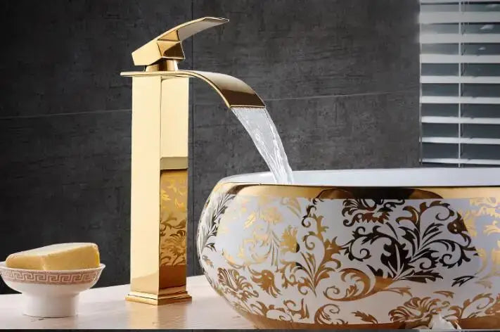 Modern gold waterfall basin faucet in gold finish flows into ornate ceramic basin with intricate gold and black floral patterns
