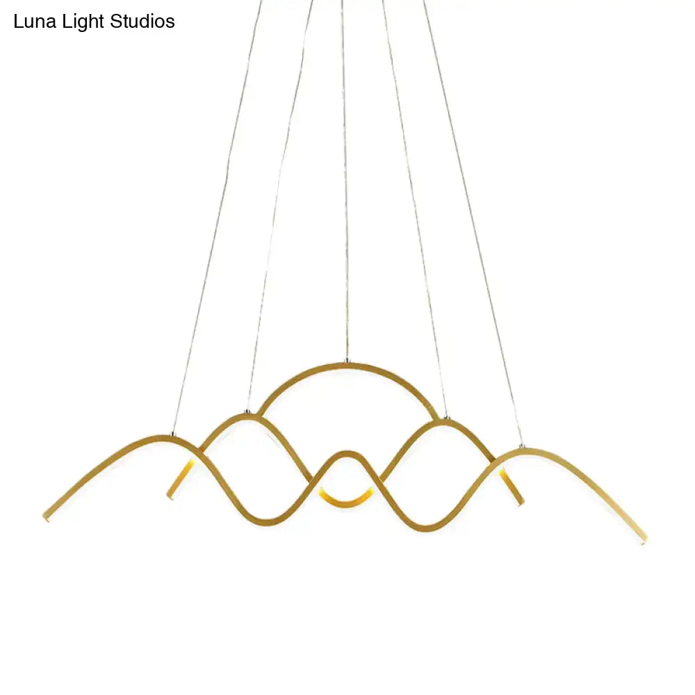 Gold-toned metal led pendant light fixture with modern wave design suspended by thin cables for dining room use