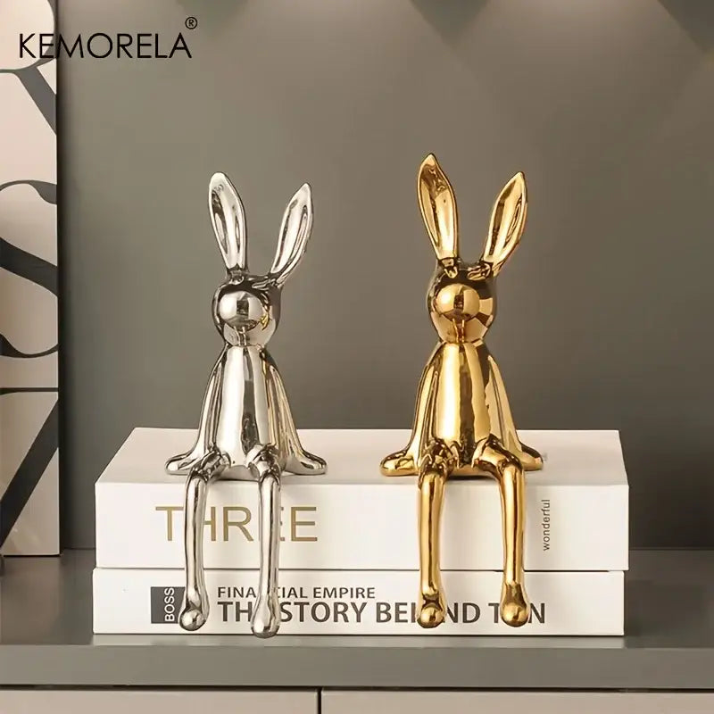 Two glossy ceramic sitting rabbit ornaments in silver and gold on stacked books for modern living room decor