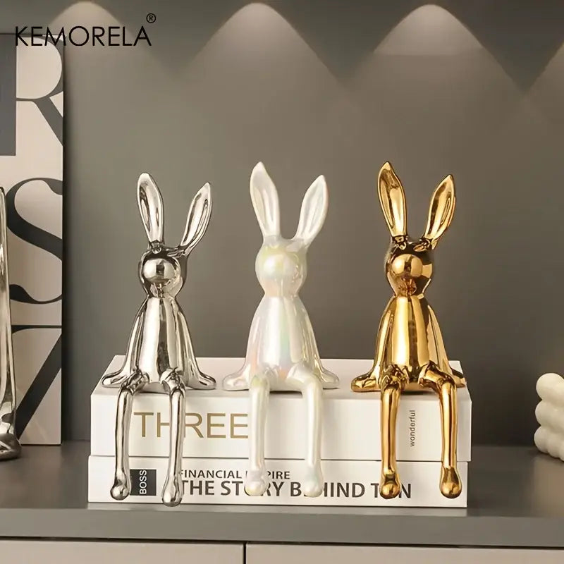 Three glossy ceramic sitting rabbit ornaments in silver iridescent white and gold on stacked books for living room decor