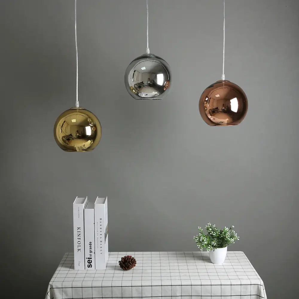 Modern golden ball glass pendant light trio with reflective gold silver and rose gold finishes hanging above table decorbites golden ball