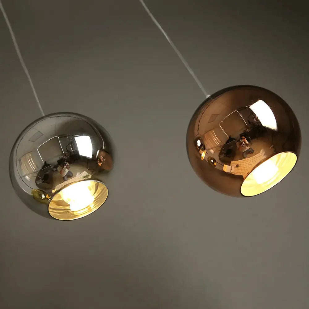 Two spherical pendant lights with polished chrome and rose gold finishes featuring illuminated golden ball glass interiors for decorbites golden ball decor