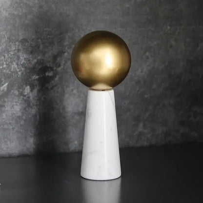 A modern golden ball spherical ornament on a white marble cone pedestal for stylish living room decor