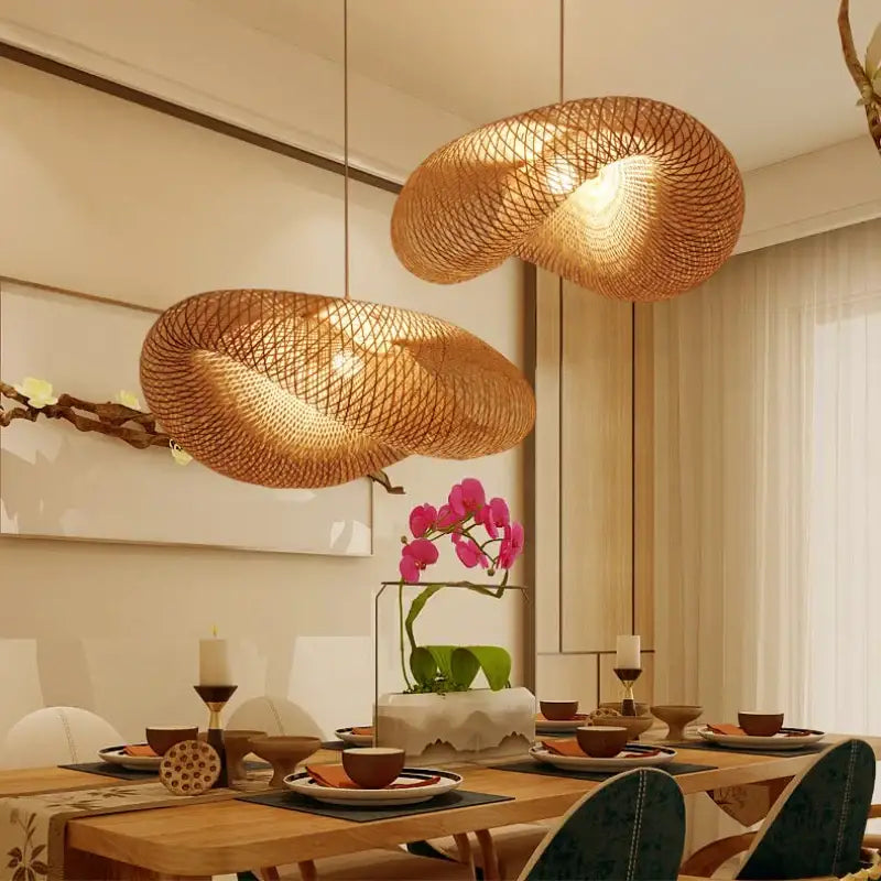 Two golden bamboo woven chandelier pendant lights hang over a dining table casting a warm glow in a tea room setting
