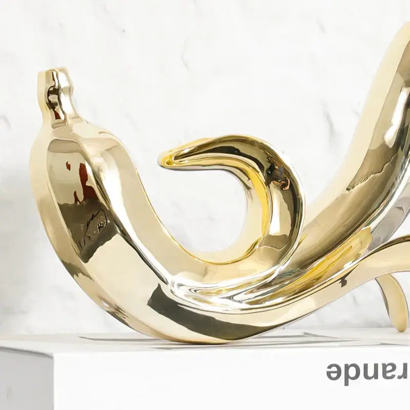 Shiny gold ceramic banana figurine with smooth reflective surface and elegant curved design for living room decor
