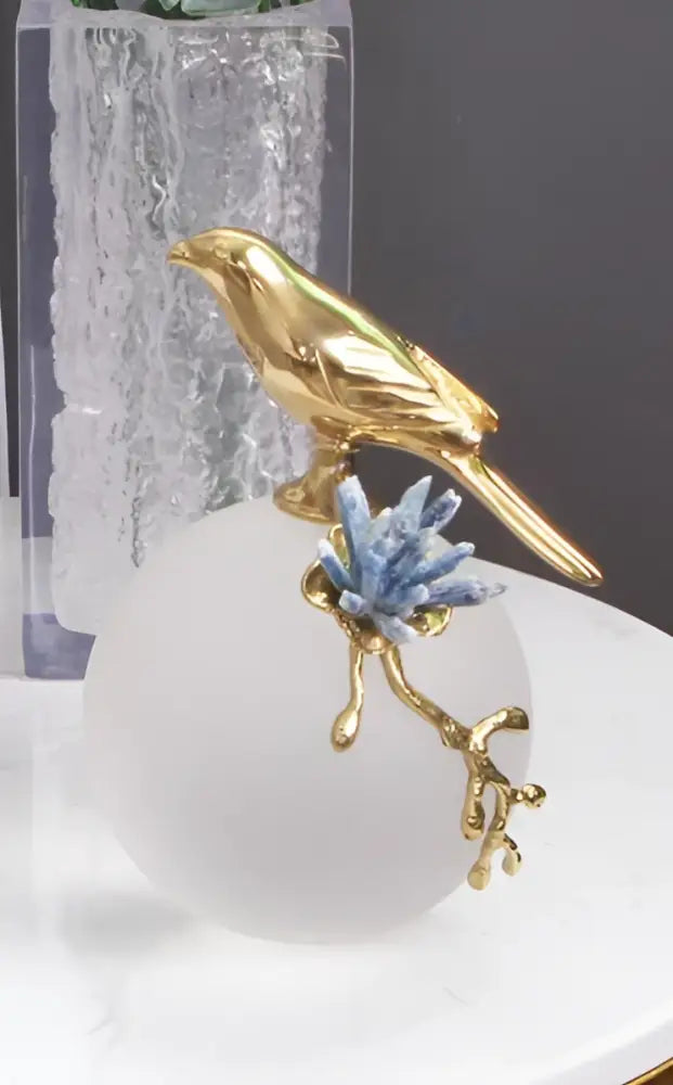 Modern golden bird brass sculpture with blue crystal accents perched on a white sphere for living room decorbites decor