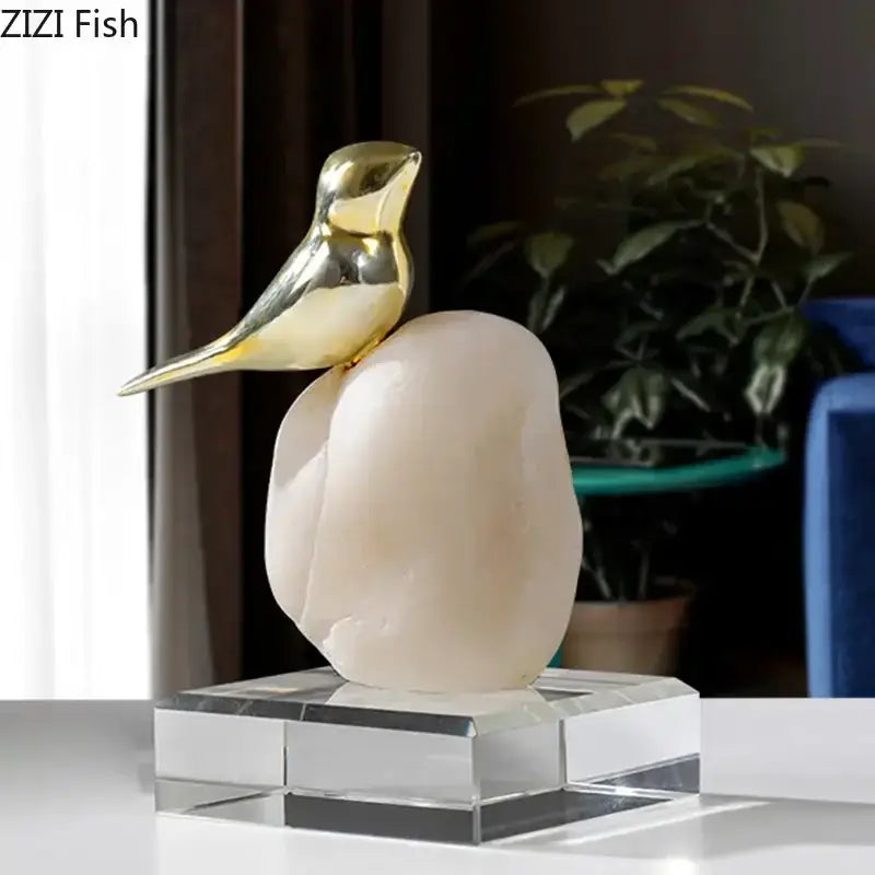 Modern golden bird statue with smooth pale pink stone base on clear acrylic pedestal for living room decor