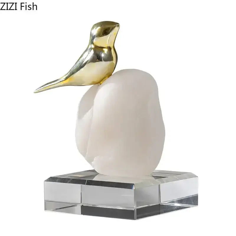 Modern golden bird statue with a gold-toned figurine perched on a milky-white stone base and clear crystal pedestal