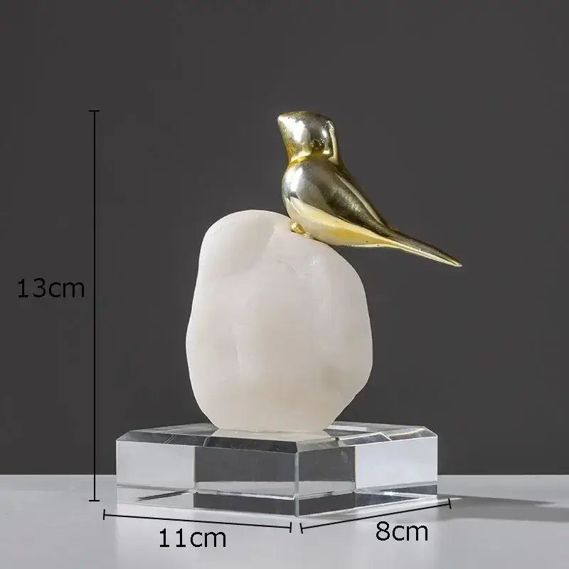 A sleek golden bird statue with a stone base on a transparent crystal pedestal for modern living room decor