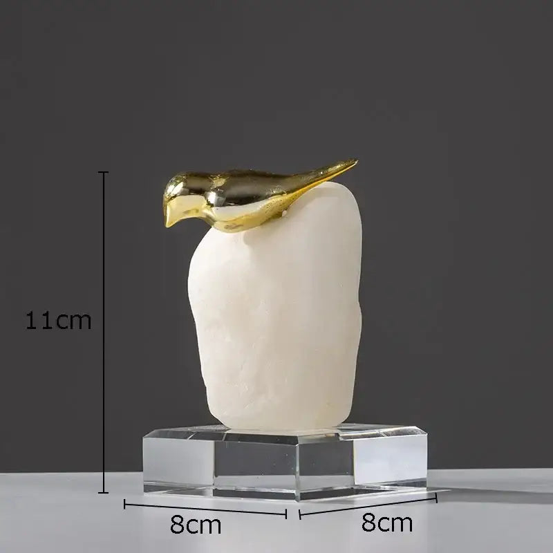 A sleek minimalist golden bird statue with a polished gold beak and head on a stone octagonal base for living room decor