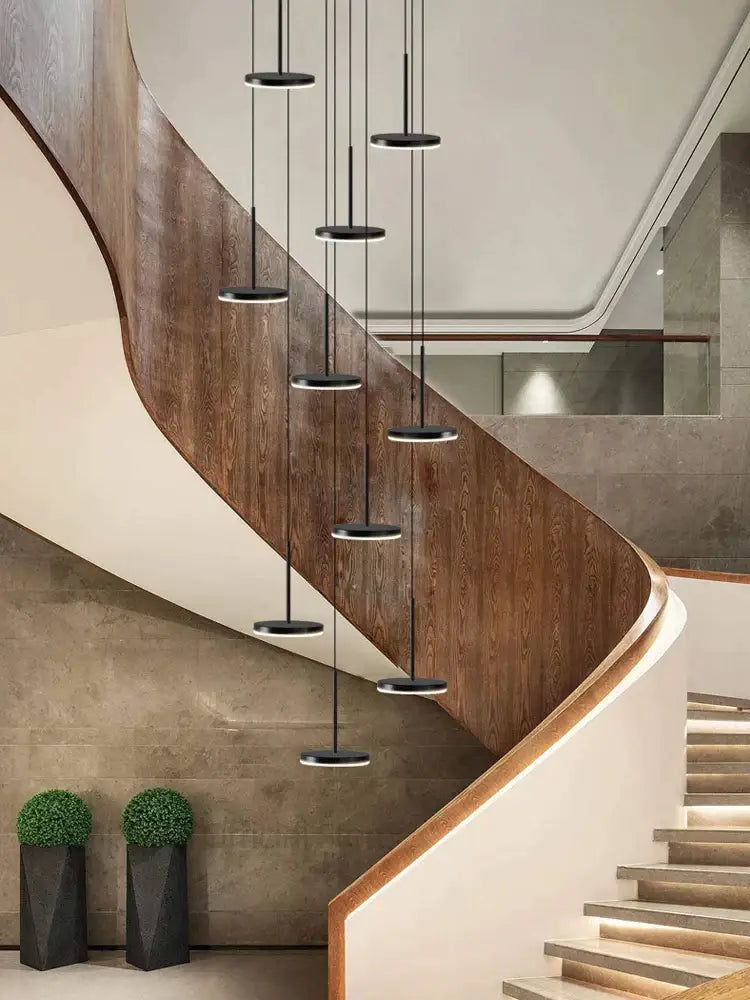 Modern golden black led long chandelier with black circular pendant lights hangs above a curved wooden staircase decorbites golden black