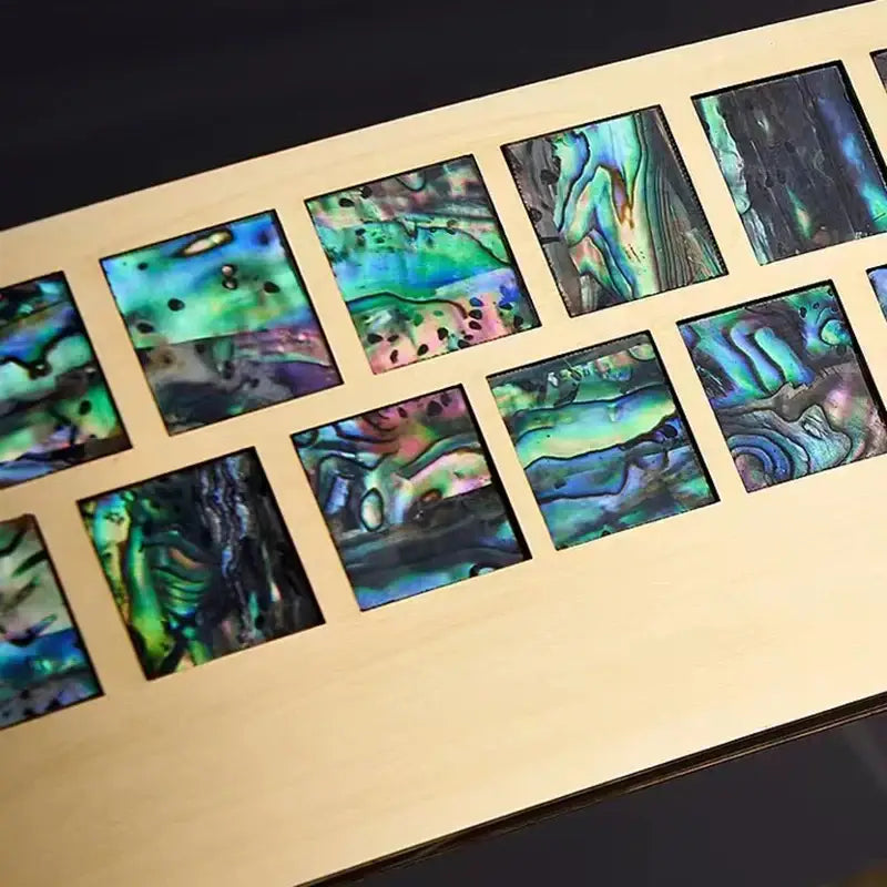 A set of square abalone inlays with iridescent green blue and purple swirls in a light wood frame for a crystal ring ceiling chandelier