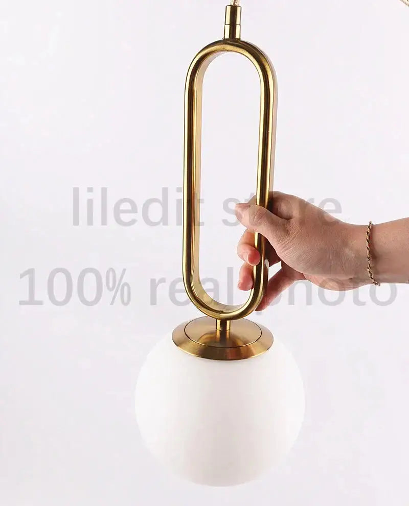 Modern golden glass ball pendant light with sleek oval metal frame and white spherical glass shade by decorbites