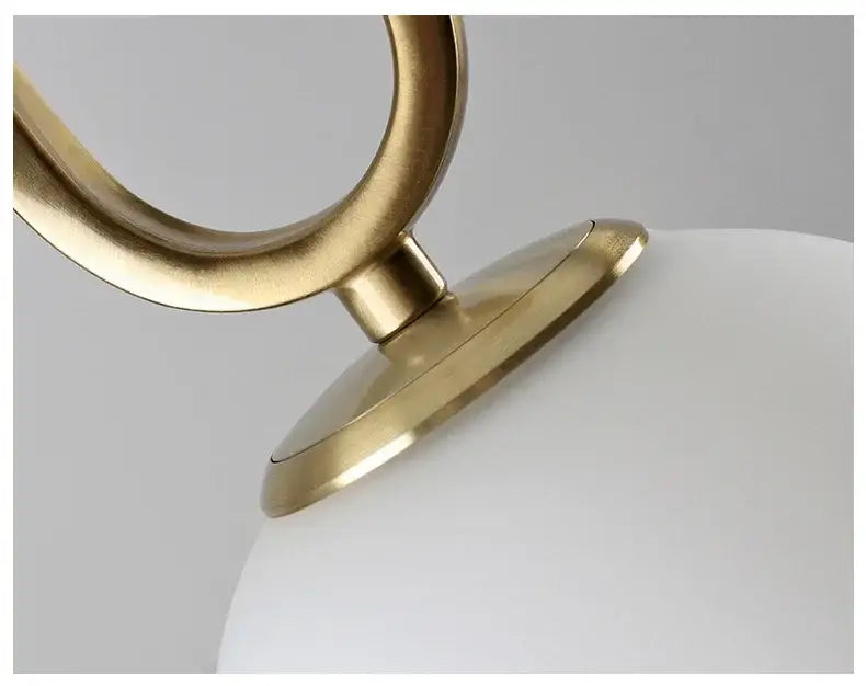 Modern golden glass ball pendant light with sleek brass finish and smooth white glass globe in an oval metal frame
