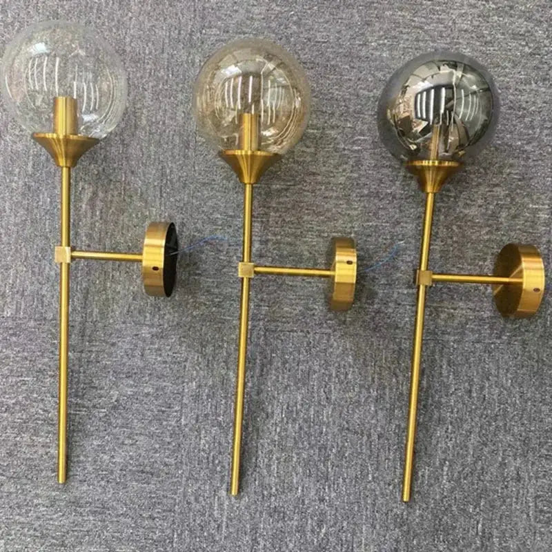 Three gold-toned wall lamps with spherical smoked glass globes and exposed filament bulbs by decorbites golden glass ball