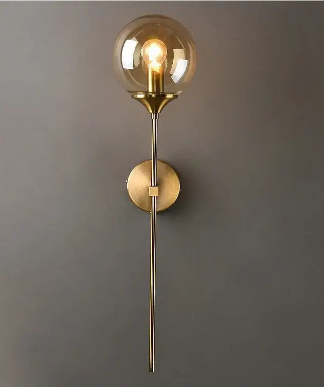 A sleek brass wall sconce with a spherical amber golden glass ball and exposed filament bulb for modern decorbites lighting