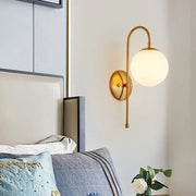 Modern golden gooseneck wall sconce with a frosted glass ball shade and curved arm for bedroom lighting