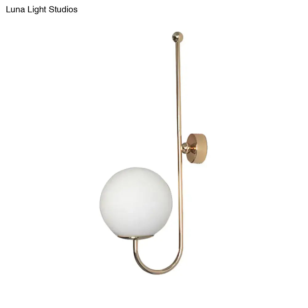 A modern golden wall sconce with a brass finish and a frosted glass ball shade for bedroom lighting