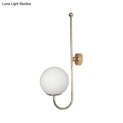 A modern golden wall sconce with a brass finish and a frosted glass ball shade for bedroom lighting