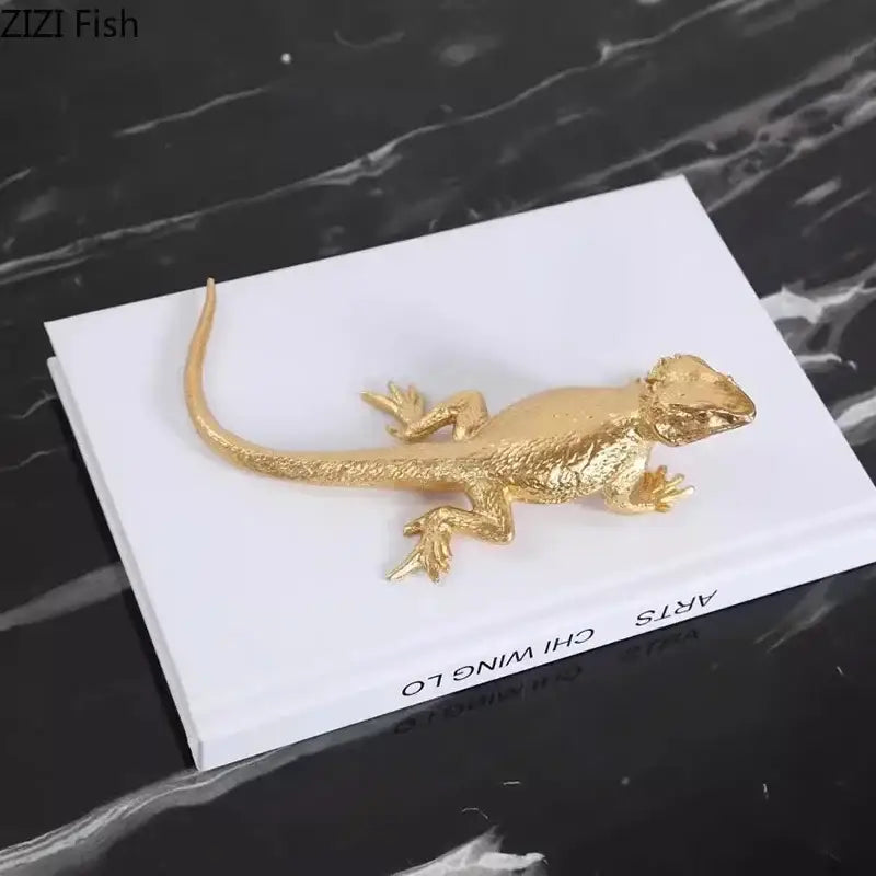 Golden lizard sculpture with textured metallic scales and detailed limbs resting on a white book for living room decor