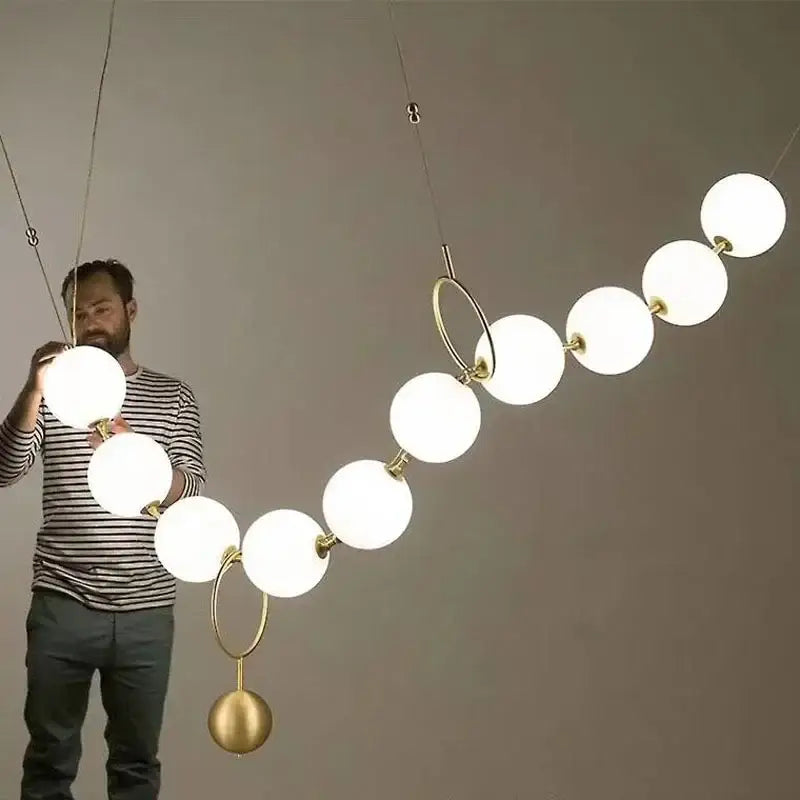 A modern golden necklace chandelier with frosted white glass globes and polished brass rings for dining room luxury lighting