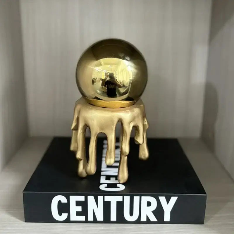 A decorbites golden octopus spherical ornament in glossy gold with a molten-metal base on a black century box for living room decor