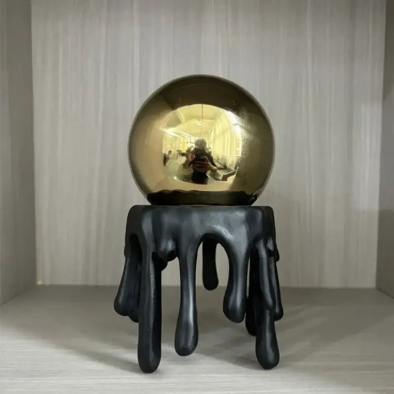 Shiny gold metallic sphere resting on a black dripping resin stand modern golden octopus spherical decorbites decor