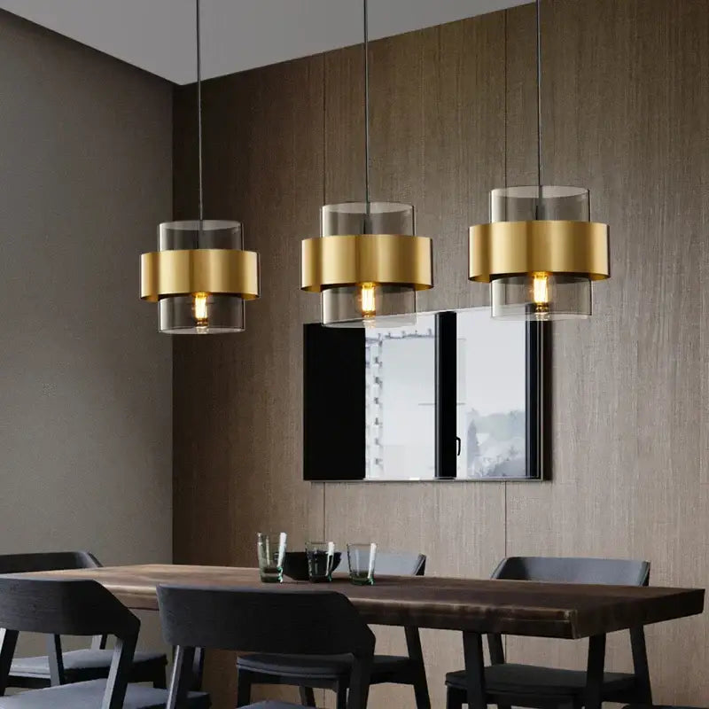 Three modern decorbites golden pendant lights with gold-finished metal rings and clear glass shades above a dining table