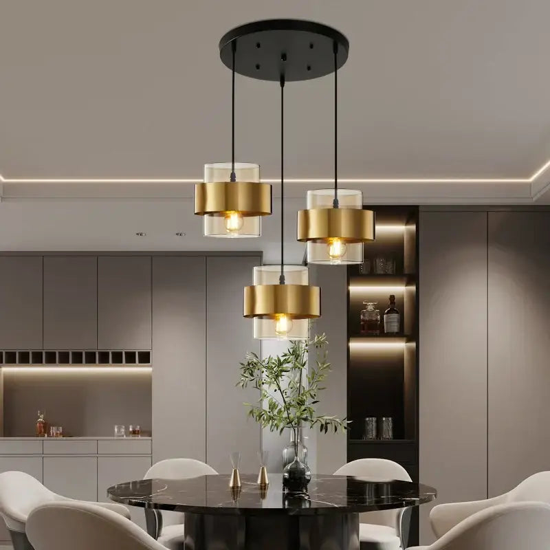Modern golden pendant lights featuring three gold-finished cylindrical shades and clear glass diffusers hanging from a black mount