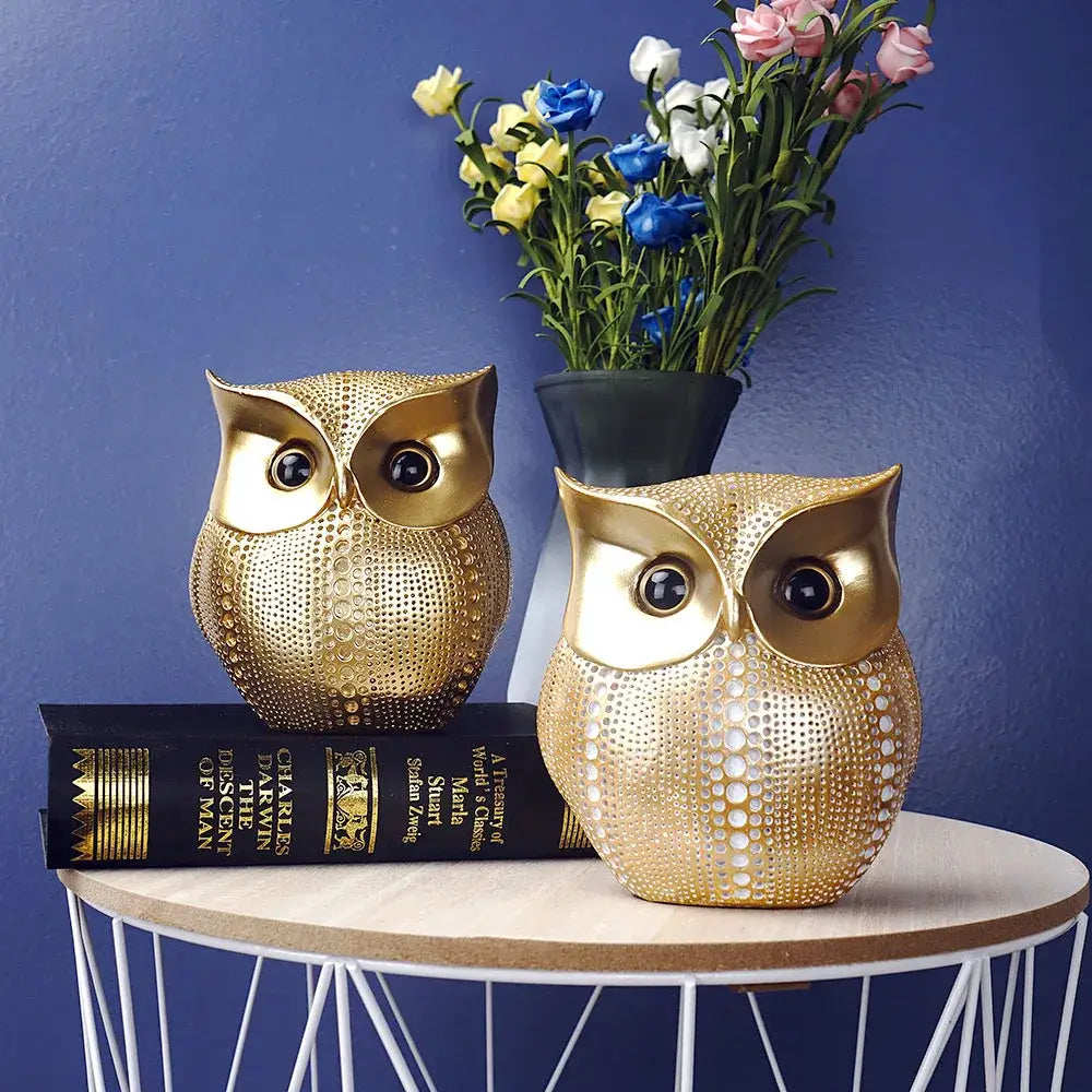 Two golden perforated owl figurines with glossy black eyes by decorbites sit on books as modern animal statues decor