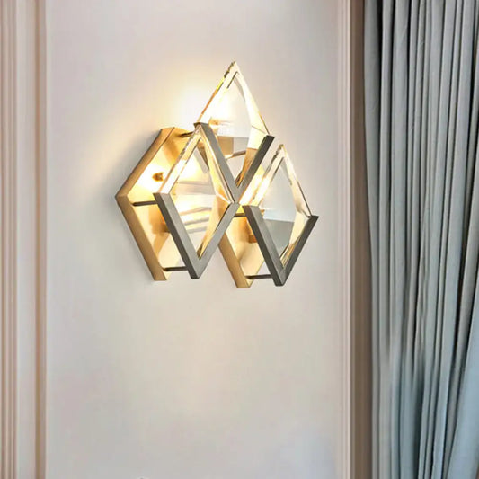 Modern style wall sconce light with clear crystal triangular facets and a dual-tone golden metallic frame for bedroom use