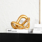 Modern golden twisted dough rope knot sculpture with metallic intertwined loops resting on a stack of books