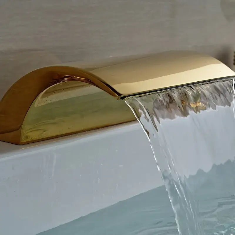 Modern golden widespread brass bathtub faucet with handheld shower featuring a gold-toned waterfall faucet design