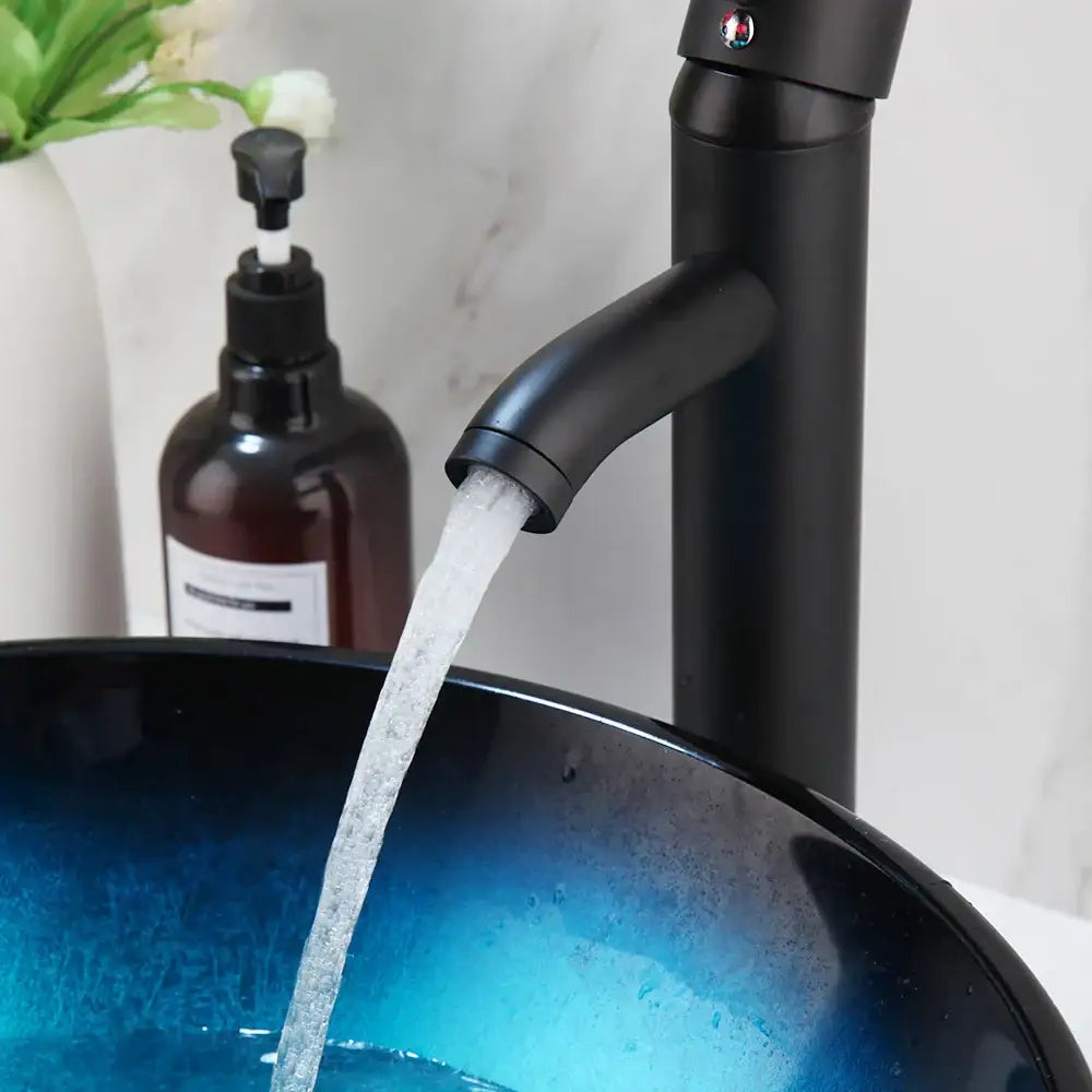 Modern gradient blue glass sink set featuring a black matte faucet flowing water into a glossy bule glass sink basin