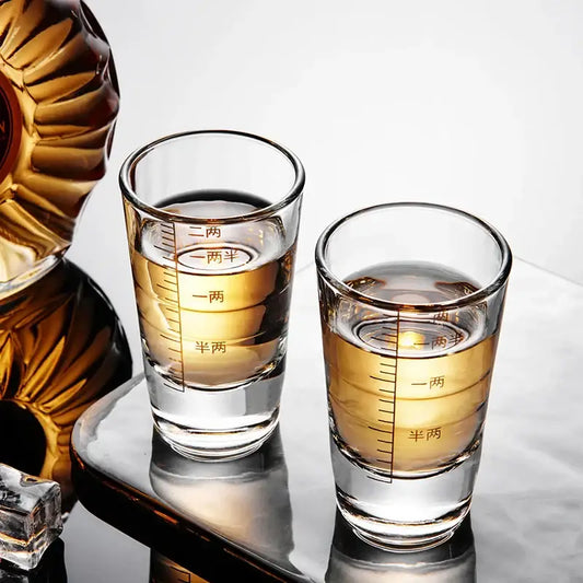 Two clear glass brandy cups with chinese measurement markings filled with golden liquid from a modern glass spirit set