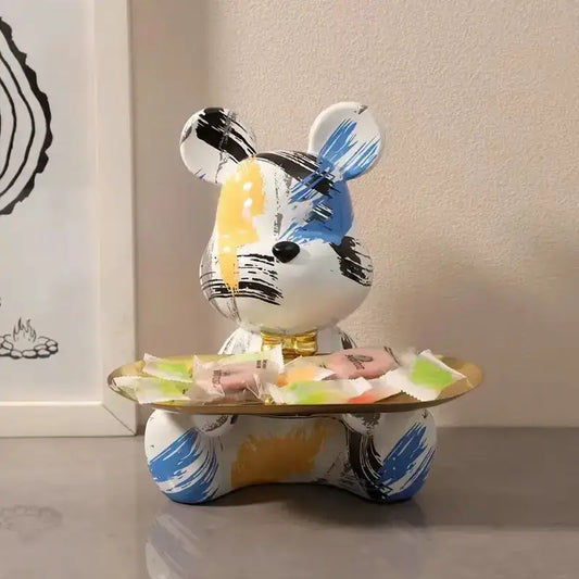 A whimsical white graffiti bear figurine with blue yellow and black patterns holds a golden tray with colorful candies